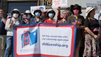 A group of newly naturalized citizens hold up an SFPCI banner for Citizenship Month
