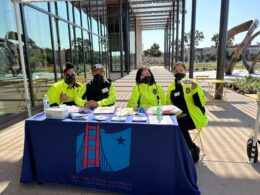 Four community ambassadors wearing bright yellow jackets smile at the registration table for the citizenship workshop.
